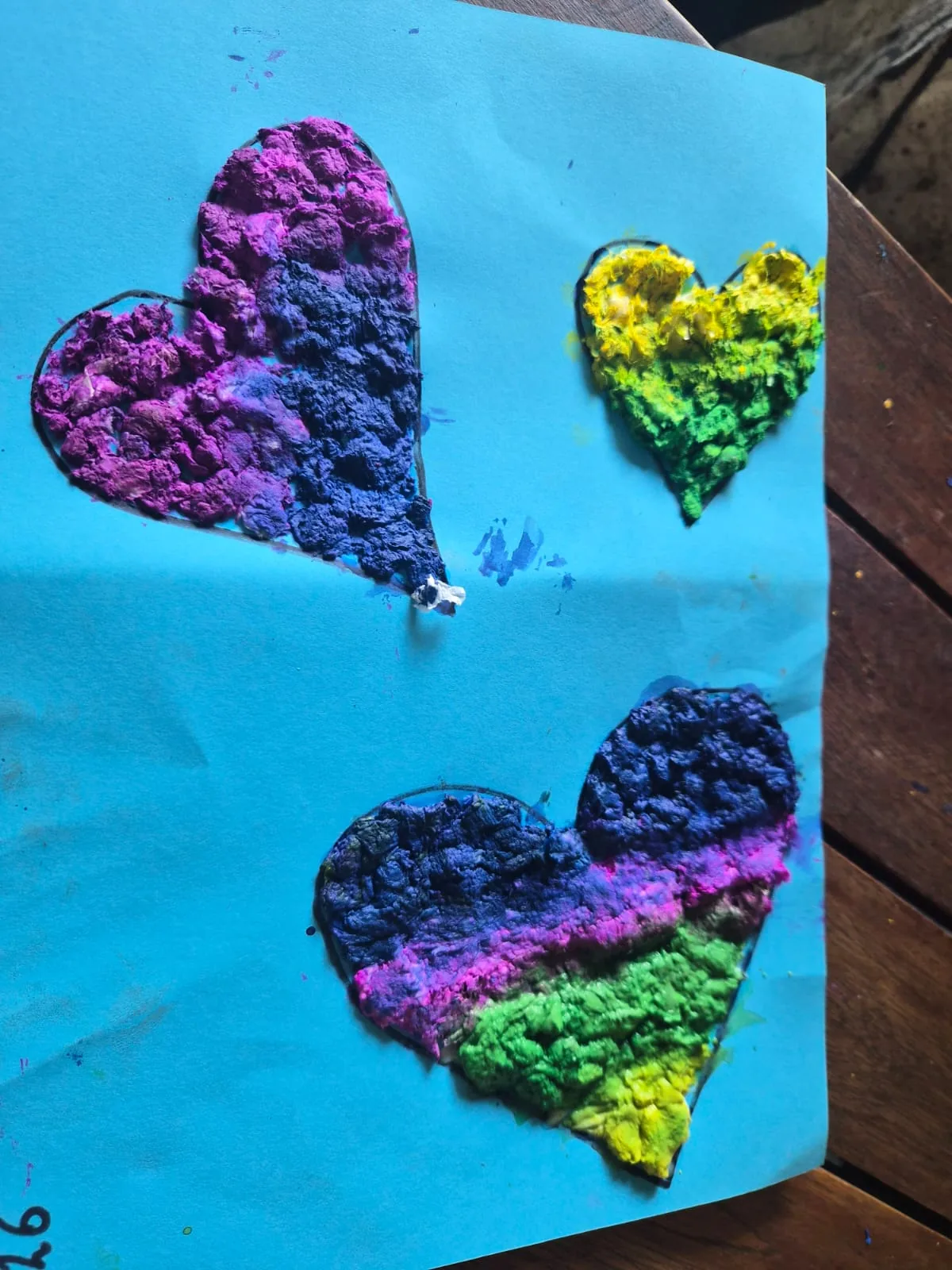 Blue sugar paper with three hearts filled in crumpled tissue paper in pink, purple, yellow and green